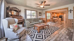 A spacious living room with a wooden floor, a ceiling fan, a piano, a sofa, a coffee table, and a dining area with wooden cabinets. - Fredricksburg Vacation Rental at 'the Loft'! (Fredericksburg)