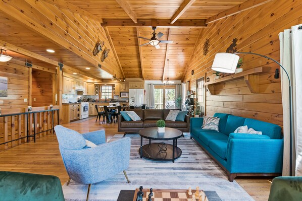 Un interior de cabaña espacioso con techo de madera, comedor, sala de estar con sofás azules y cocina.