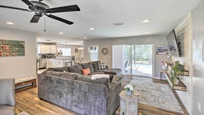 A spacious living room with a gray sectional sofa, a ceiling fan, and a kitchen in the background. - Lavish Holiday Home w/ Lanai & Heated Outdoor Pool (Holiday)
