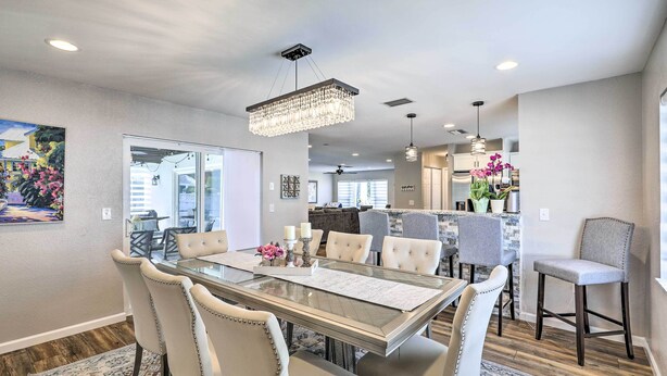 A dining area with a glass-top table, cushioned chairs, a chandelier, and a kitchen in the background. - Lavish Holiday Home w/ Lanai & Heated Outdoor Pool (Holiday)