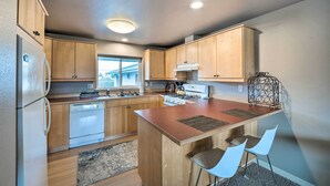 A modern kitchen with wooden cabinets, a central island, and a window providing natural light. - Apartment w/ Gas Fireplace ~ 1/2 Mi to Beach! (Anacortes)