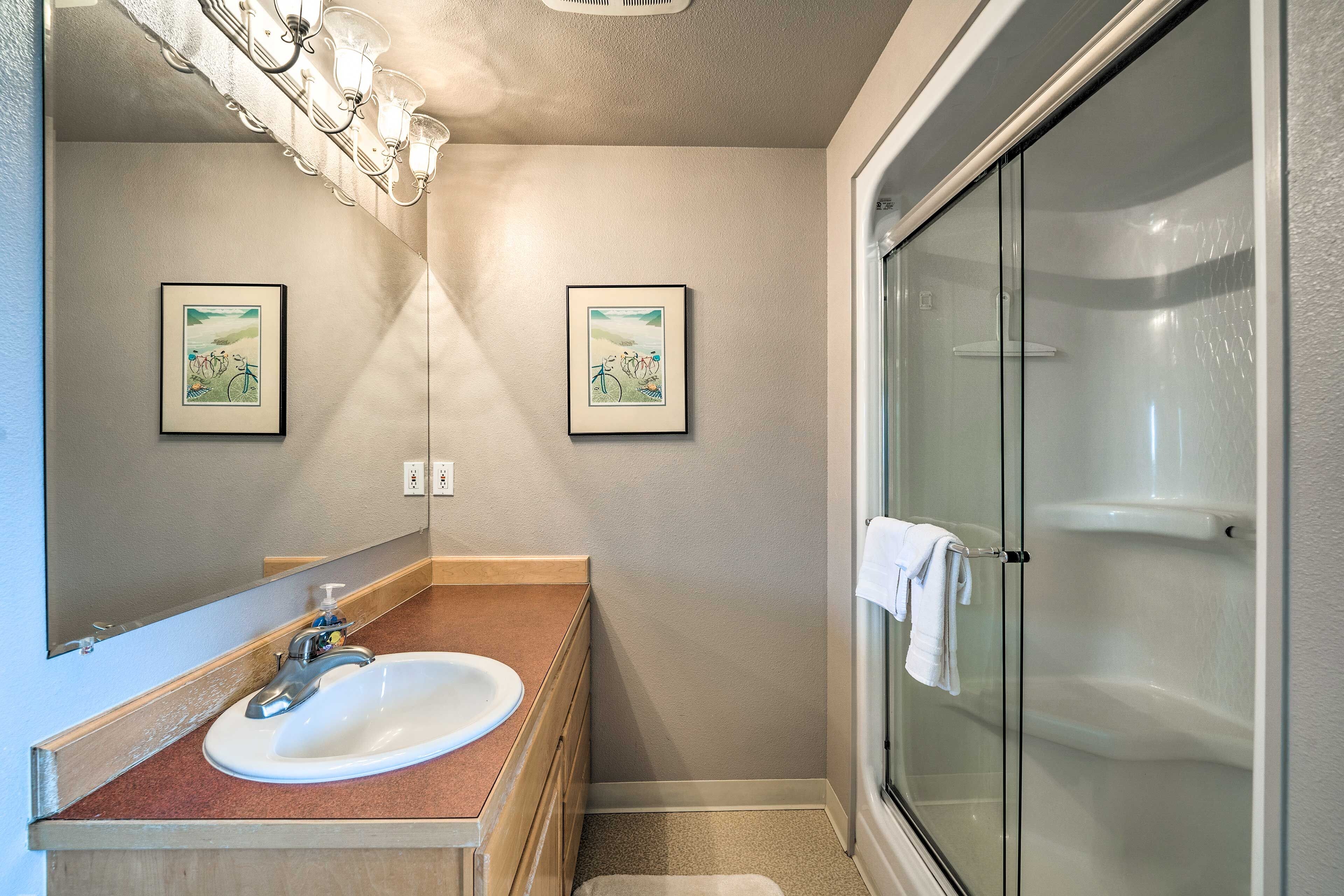 A bathroom with a sink, mirror, and shower. There are two framed pictures on the wall.