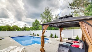 Un jardin avec une piscine, des chaises longues, un espace salon couvert et une pergola.
