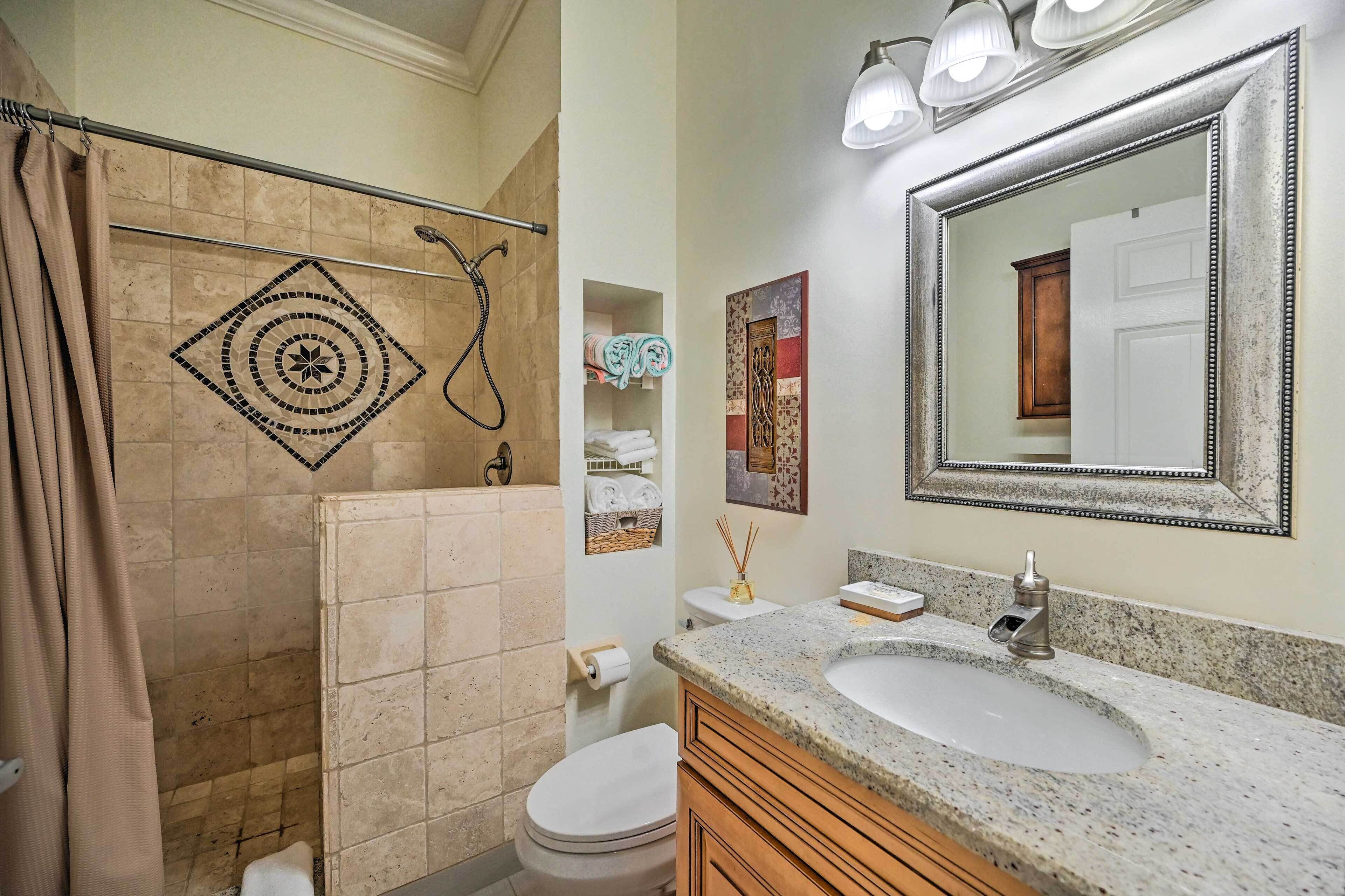 A bathroom with a shower, toilet, sink, and a large mirror.