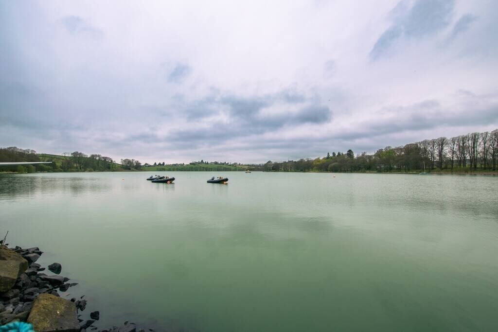 A calm lake with boats, surrounded by trees and a cloudy sky.