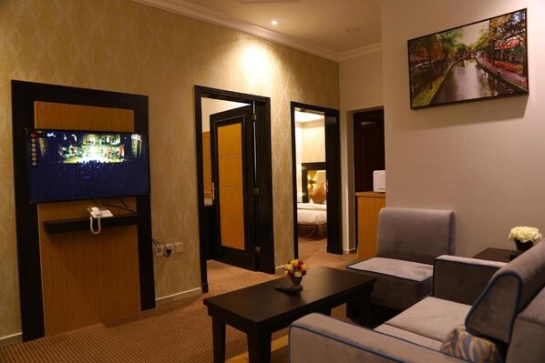 A hotel room with a TV, seating area, and a bed. - Golden Rest Serviced Apartments (Al Khobar)