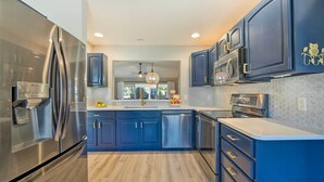 A modern kitchen with stainless steel appliances, dark blue cabinets, and a central island. - Sunny Home w/ Golf Cart in The Villages! (The Villages)