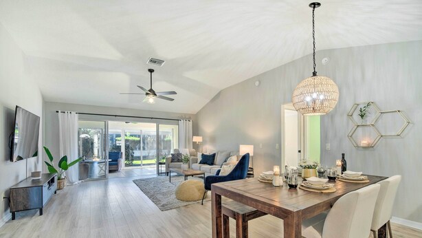 A spacious living area with a wooden dining table, a ceiling fan, and a large chandelier. - Sunny Home w/ Golf Cart in The Villages! (The Villages)