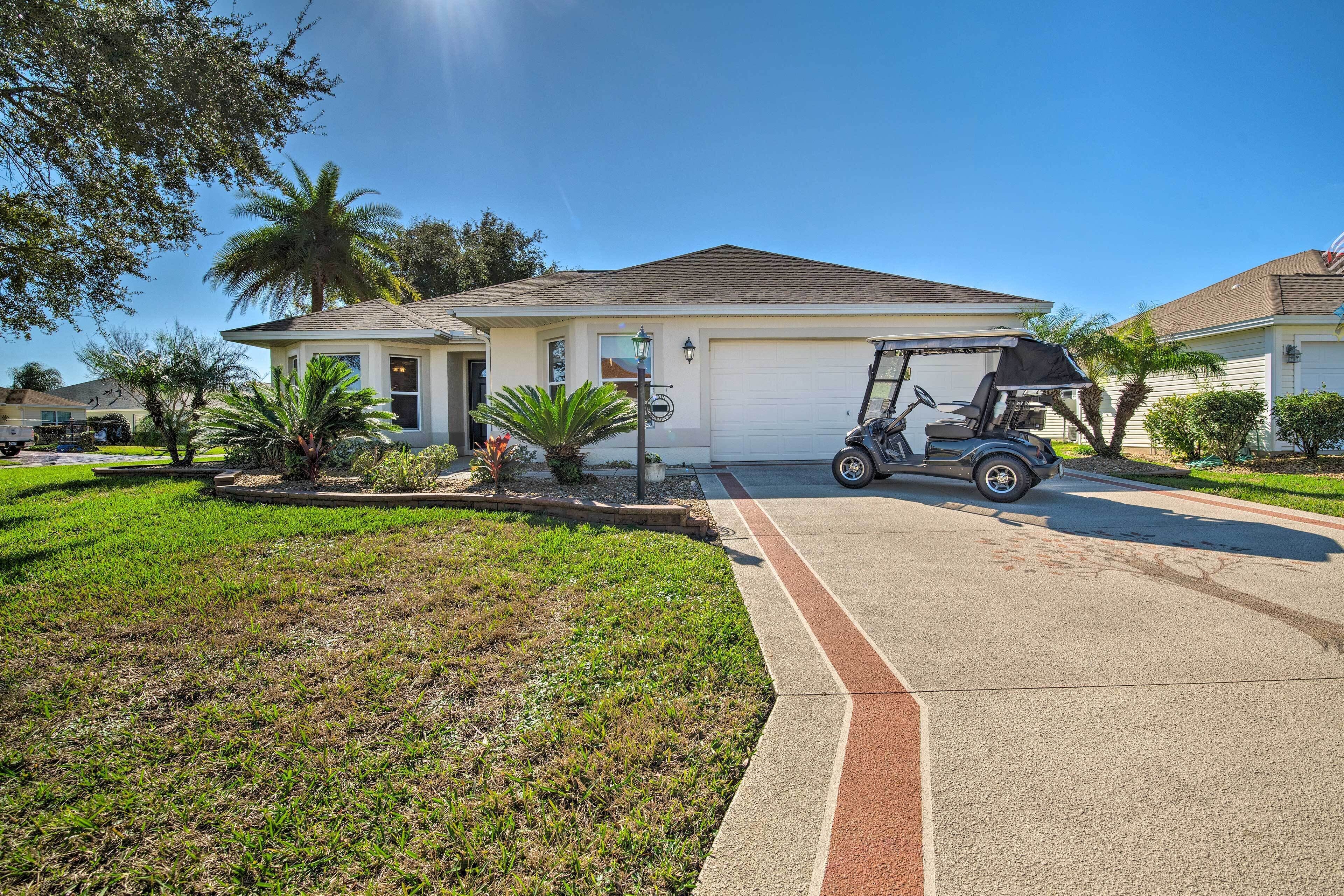 A single-story house with a garage, surrounded by well-maintained lawns and palm trees.