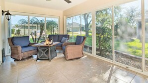A sunroom with wicker furniture, a ceiling fan, and large windows offering a view of a residential area. - Sunny Home w/ Golf Cart in The Villages! (The Villages)