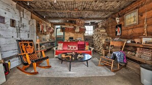 A rustic cabin interior with a red sofa, a rocking chair with a 'Vicky' sign, a wooden table, and a stone wall with a framed picture. - Colorado Mountain Cabin Near National Forest! (Guffey)