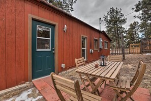 A red wooden building with a green door, a small porch with wooden benches, and a table with a lantern. - Colorado Mountain Cabin Near National Forest! (Guffey)