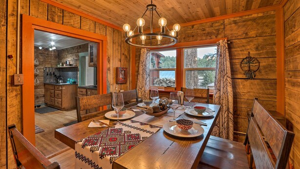 A wooden dining area with a chandelier, a large window, and a view of the outdoors. - Colorado Mountain Cabin Near National Forest! (Guffey)