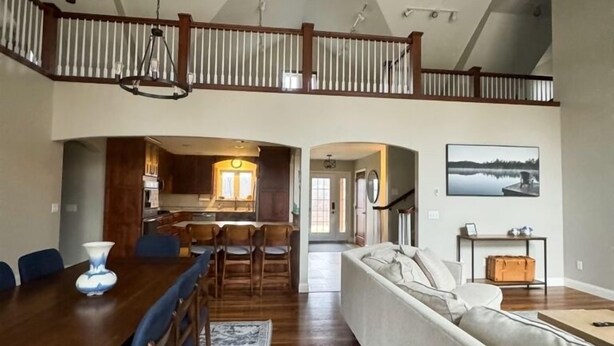 A spacious living area with a high ceiling, wooden flooring, a dining table with chairs, a sofa, and a staircase leading to an upper level. - An Oasis on the Lake (New London)