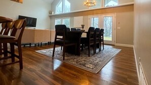 A spacious dining area with a high ceiling and large windows, wooden flooring, and a chandelier. - An Oasis on the Lake (New London)