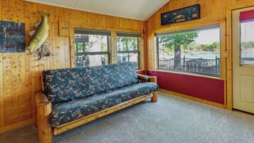 A wooden interior with a sofa, a fish mounted on the wall, and a view of the outside.