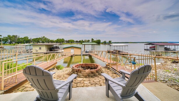 A deck with Adirondack chairs overlooking a body of water, a fire pit, and dock structures. - Grand Lake Waterfront Home: 2 Boat Docks (Grove)