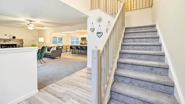 A staircase with a grey carpet and white railing, leading to a second-floor landing with a decorative wall piece. - 3 Mi to Kalahari: Pocono Summit Home w/ Game Room! (Pocono Summit)
