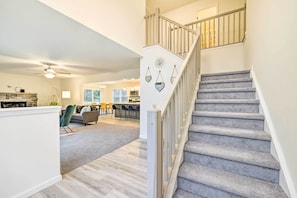 Un escalier recouvert d’une moquette grise et doté d’une rampe blanche, menant à un palier du deuxième étage où est accroché un élément décoratif au mur.