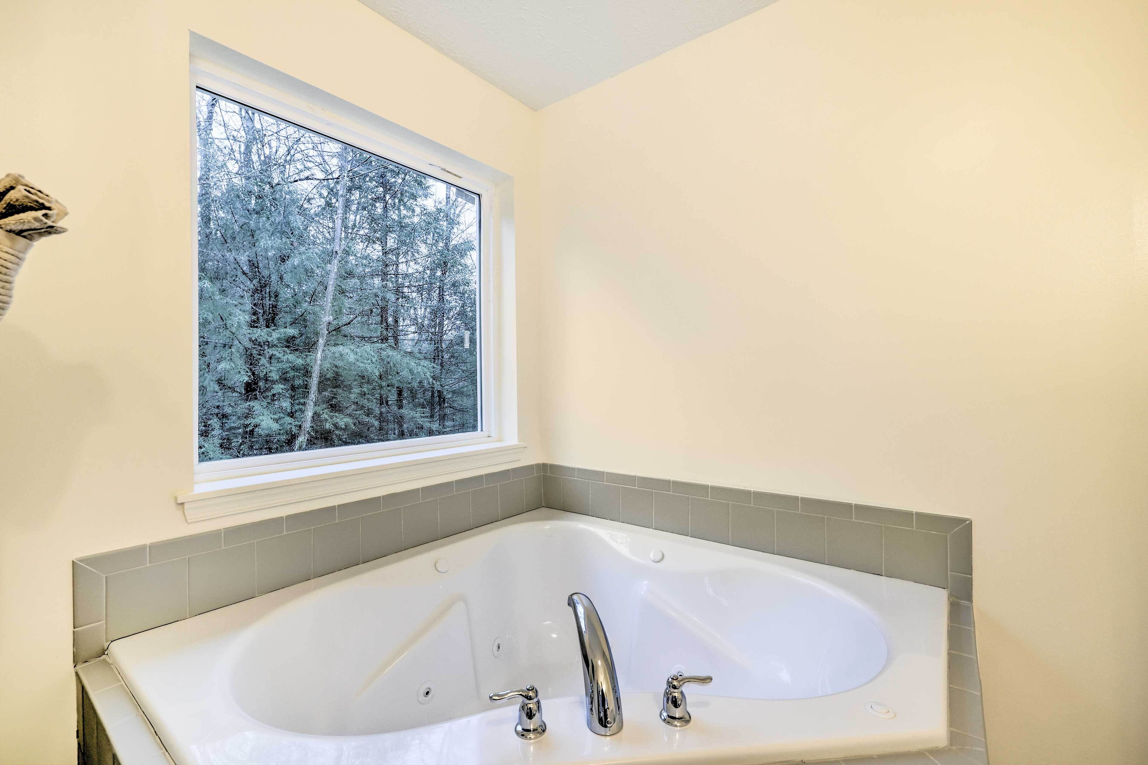 Un bagno con una vasca da bagno ampia, una finestra vista foresta e un porta asciugamani.