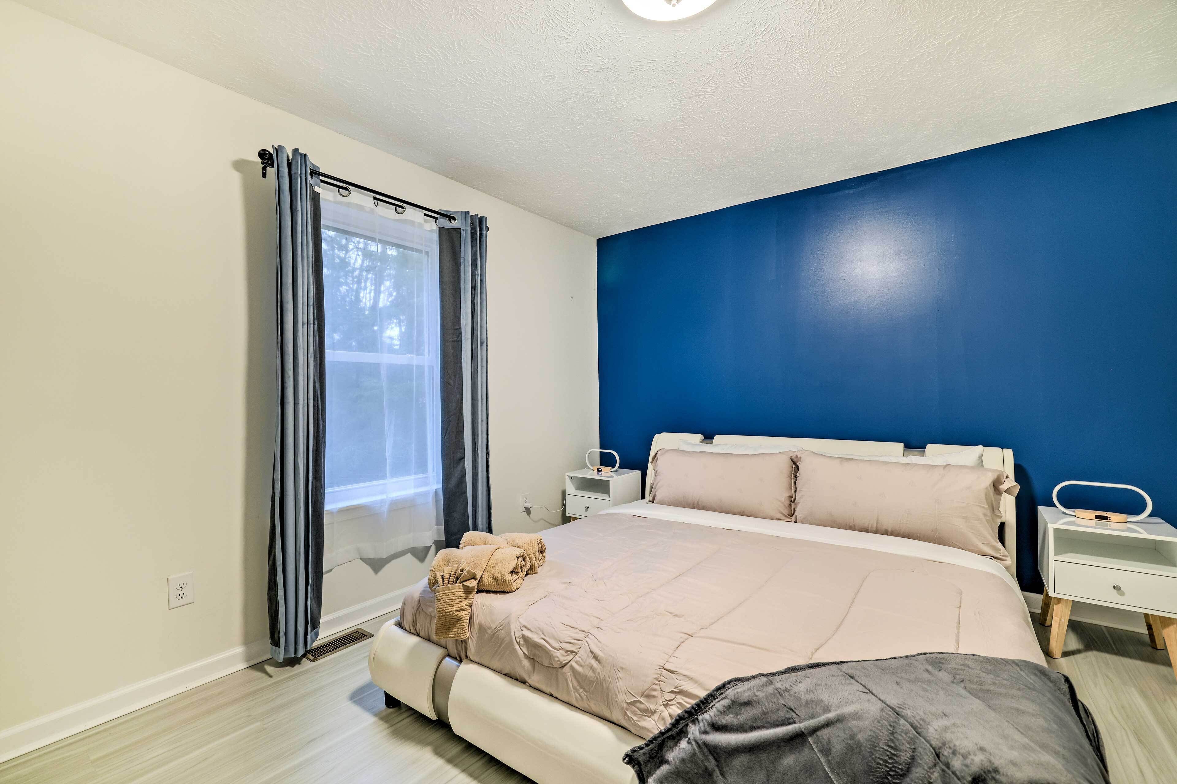 A bedroom with a bed, a nightstand, a window with curtains, and a blue accent wall.