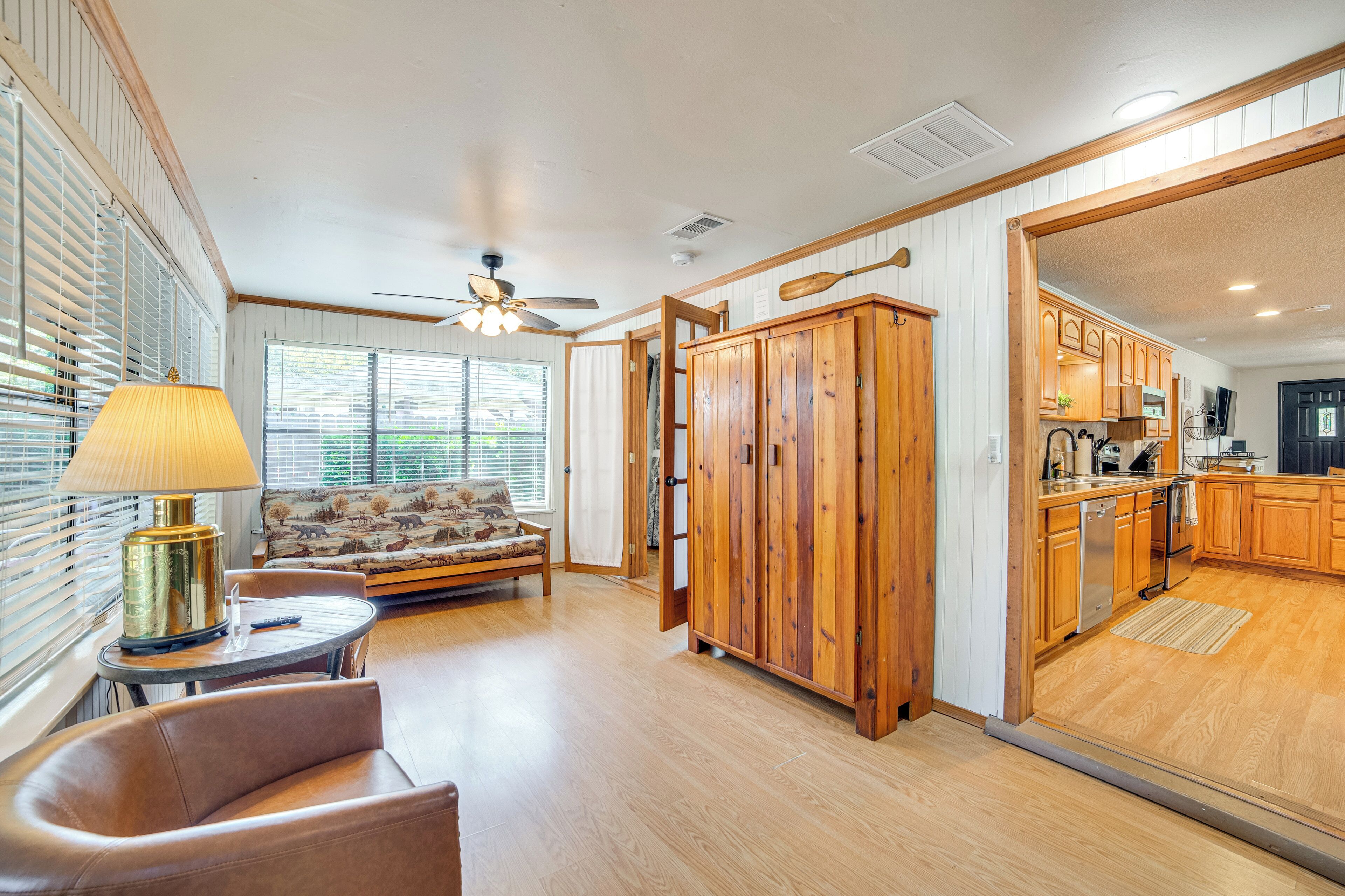 A spacious living area with a sofa, a table with a lamp, wooden cabinets, and a kitchen area with wooden cabinets and appliances.