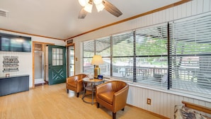 A room with wooden flooring, a ceiling fan, a green door, a table with chairs, and large windows with blinds. - Spacious Deck: Waterfront Home in Gun Barrel City! (Mabank)