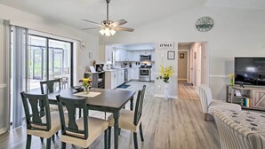 A modern kitchen with white cabinets, a dining area with a wooden table and chairs, and a living room with a sofa and a TV. - Bright Sebastian Home w/ Pool ~ 7 Mi to Beach! (Sebastian)