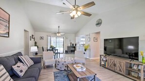 A spacious living room with a grey sofa, ottoman, and coffee table, a TV on a wooden stand, and a ceiling fan. - Bright Sebastian Home w/ Pool ~ 7 Mi to Beach! (Sebastian)