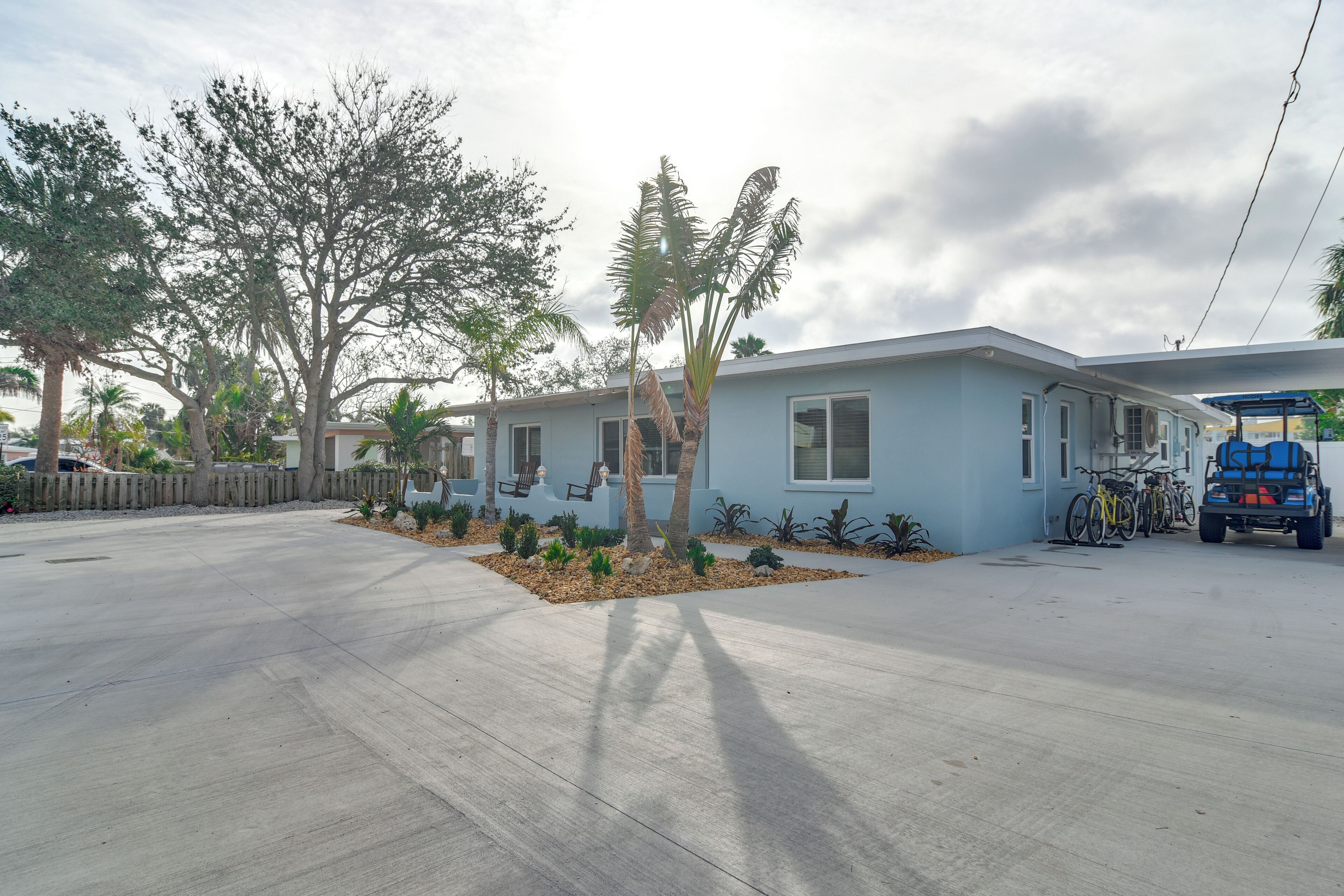 Un quartier résidentiel avec une maison bleu clair, une clôture en bois et un véhicule bleu garé.