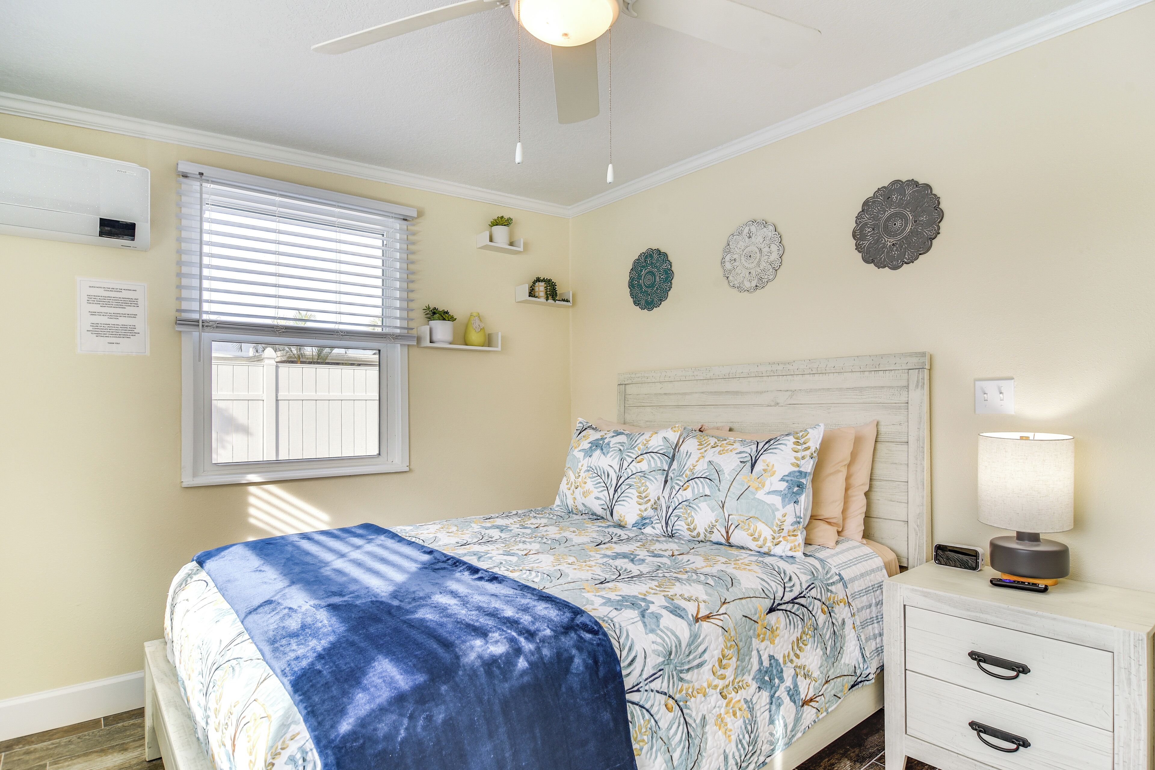 Un dormitorio con cama, mesita de noche, lámpara y elementos decorativos en la pared.