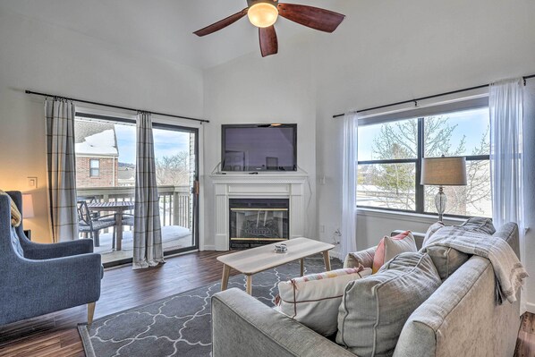 A living room with a fireplace, a television, a ceiling fan, and a view of the outside. - Branson Vacation Rental w/ Resort Amenities (Branson)