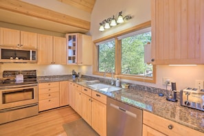 A modern kitchen with wooden cabinets, stainless steel appliances, granite countertops, and a large window providing natural light. - Ski + Bike: Home w/ Deck & Hot Tub in Granby! (Granby)