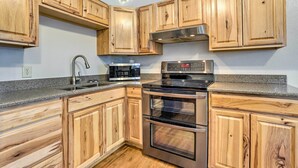 Eine Küche mit Holzausstattung, einem Edelstahlbackofen, einer Mikrowelle und einer Granitarbeitsplatte.