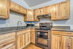 A kitchen with wooden cabinets, a stainless steel oven, a microwave, and a granite countertop. - Alaskan Retreat Near Matanuska Glacier & River! (Sutton)