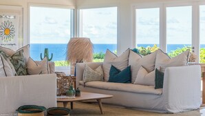 A living room with a white sofa, teal cushions, and a view of the ocean. - Villa Poppy | Ocean View - Located in  Tropical Mont Jean with Private Pool (Montjean)