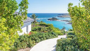 A coastal view with a pathway leading to a white building, surrounded by lush greenery and overlooking the ocean. - Villa Poppy | Ocean View - Located in  Tropical Mont Jean with Private Pool (Montjean)