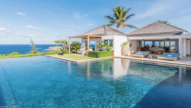 A modern resort with a large infinity pool, outdoor seating, and a view of the ocean. - Villa Poppy | Ocean View - Located in  Tropical Mont Jean with Private Pool (Montjean)