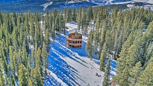 A lodge surrounded by snow-covered ground and tall pine trees, with a mountain range in the background. - 26-0086 Fairplay Cabin w/ Hot Tub! (Fairplay)