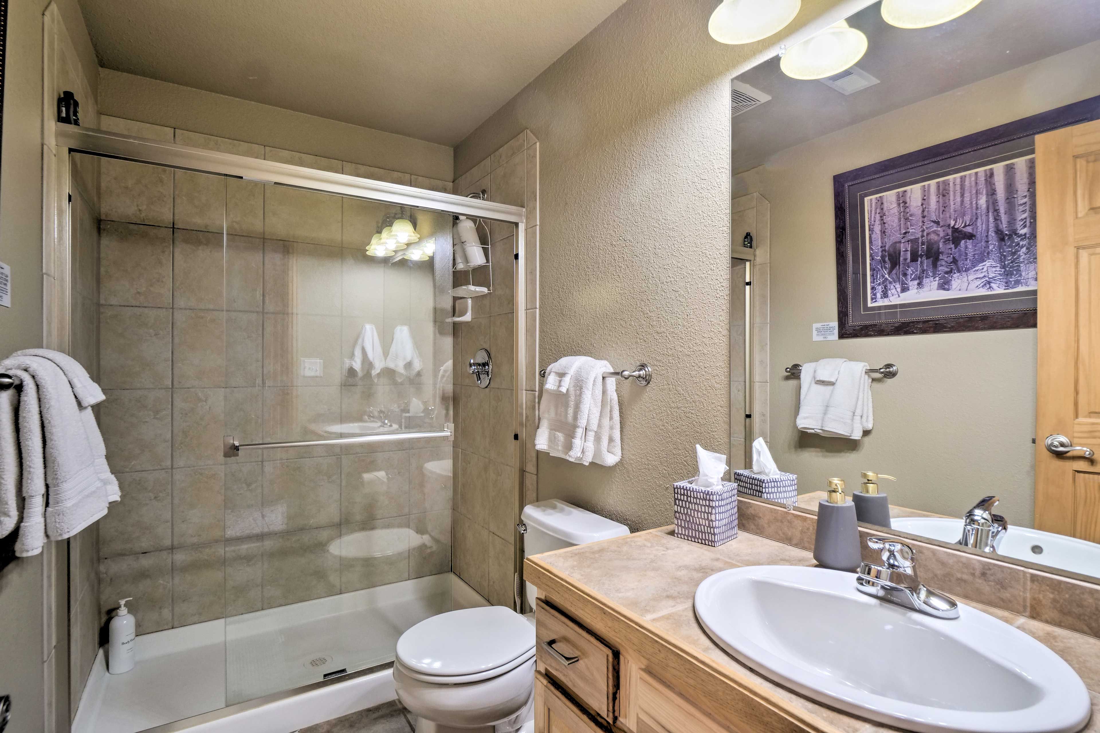 A modern bathroom with a glass-enclosed shower, a toilet, a sink with a mirror, and a framed picture on the wall.