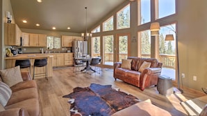 A spacious living area with a large wooden dining table, leather sofa, and a cowhide rug. There are multiple windows providing natural light and a view of the outdoors. - 26-0086 Fairplay Cabin w/ Hot Tub! (Fairplay)