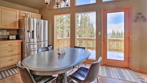 A kitchen with a stainless steel refrigerator, a dining table with chairs, and large windows offering a view of trees and a deck. - 26-0086 Fairplay Cabin w/ Hot Tub! (Fairplay)