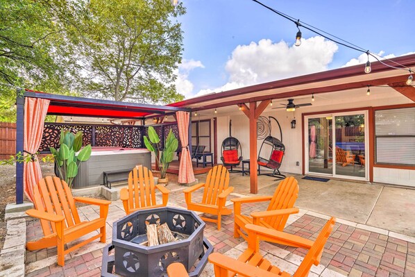 Une terrasse extérieure avec des fauteuils Adirondack orange, un foyer et un espace salon couvert équipé d’un ventilateur de plafond.
