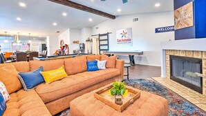 A modern living room with a sectional sofa, a coffee table with a floral arrangement, a fireplace, and a 'Welcome' sign. - San Antonio Home w/ Hot Tub & Arcade Games! (San Antonio)