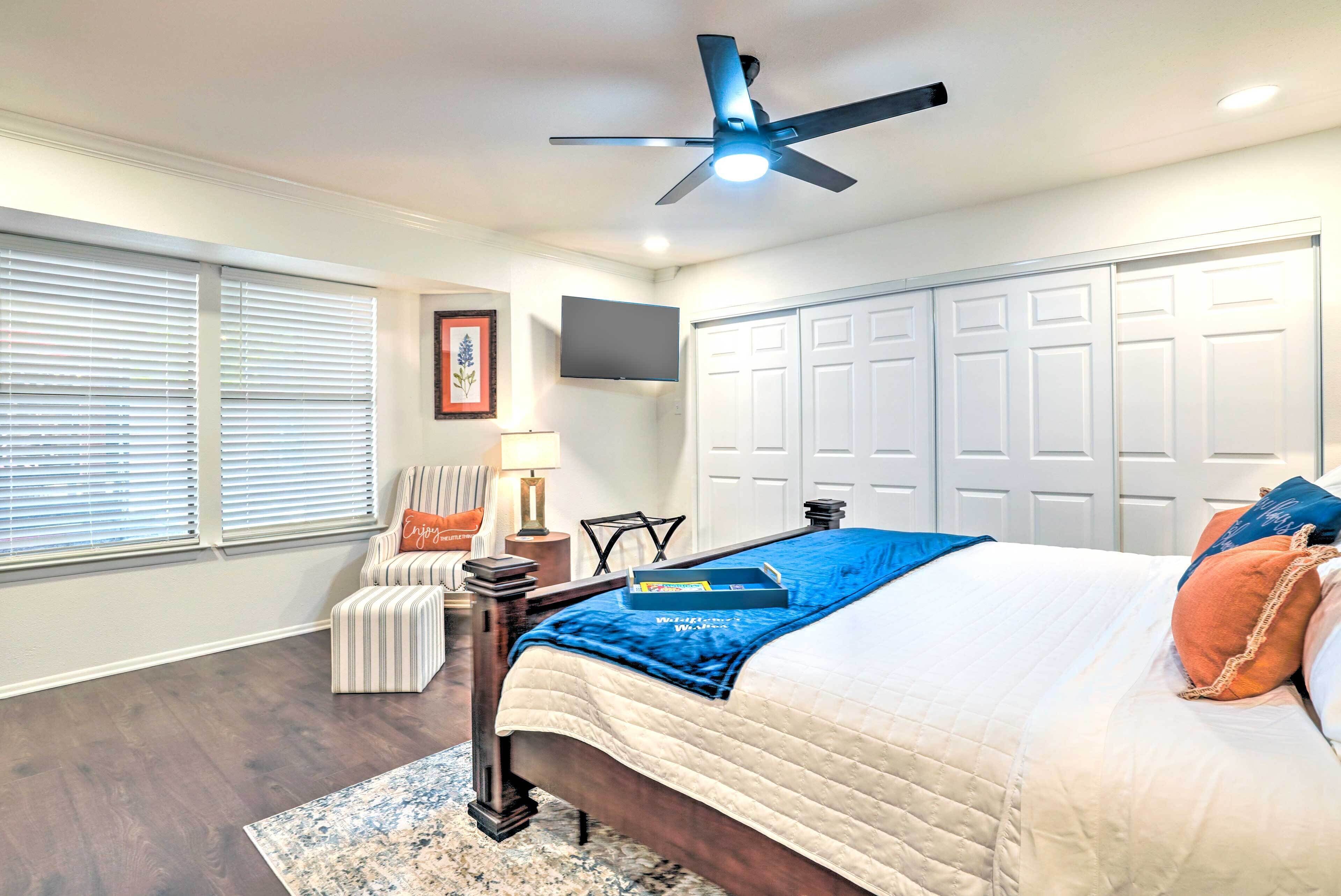 A bedroom with a bed, a ceiling fan, a TV, a chair, and a desk.