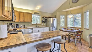 Une cuisine avec des meubles de rangement en bois, un réfrigérateur en acier inoxydable, un îlot central en bois avec des tabourets, et une table à manger avec des chaises.
