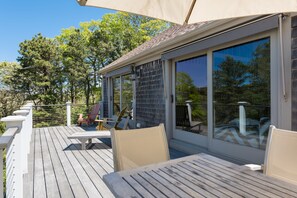 A wooden deck with outdoor furniture, large windows, and a view of trees. - Peaceful Nauset Beach Sanctuary (Orleans)