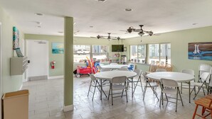 A spacious room with a large round table, multiple chairs, ceiling fans, and a television. - 'sea-king Sol' Ocean-view Condo in Port Aransas! (Port Aransas)