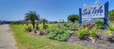 Señal de Sea Isle Village con cielo despejado y zona verde con plantas.
