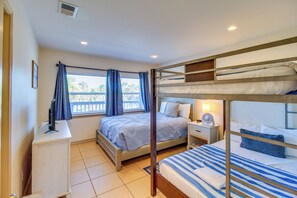 Une chambre avec des lits superposés, un bureau, une chaise, une table de chevet avec une lampe et une fenêtre avec des rideaux.